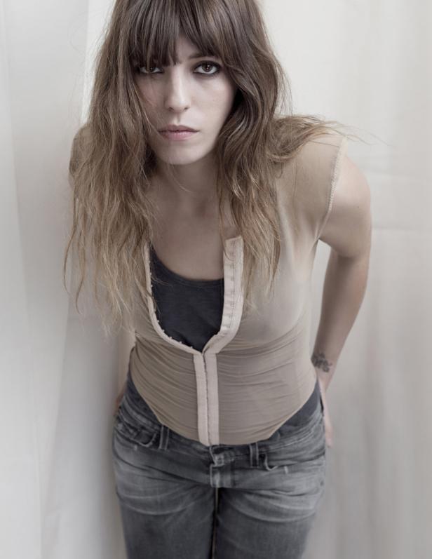 Eine Frau mit langen, gewellten Haaren und dunklem Make-up blickt in die Kamera.