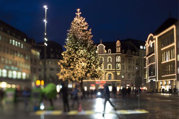 Ein großer, beleuchteter Weihnachtsbaum auf einem Platz in der Stadt bei Nacht.