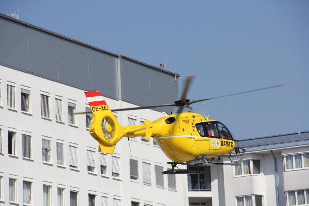 Ein gelber Rettungshubschrauber des ÖAMTC vor einem Gebäude.