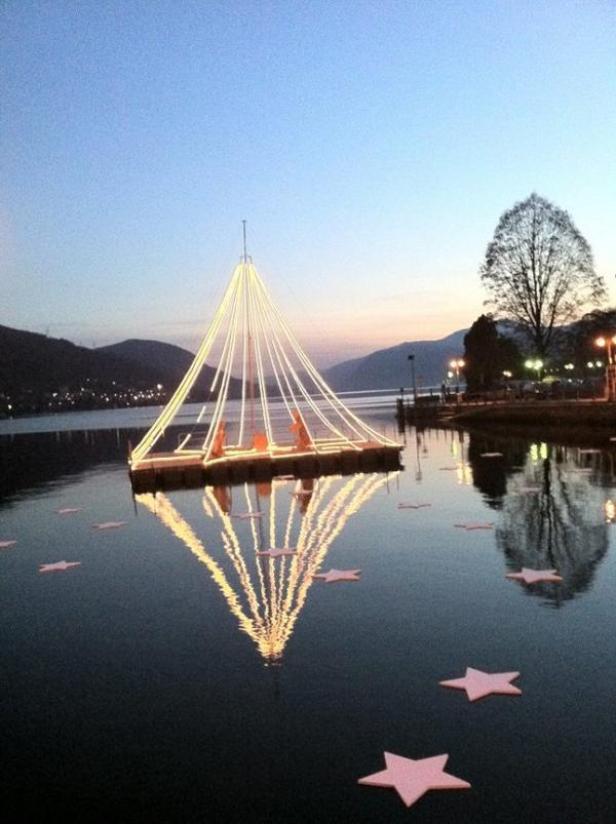 Ein beleuchteter Weihnachtsbaum auf einem See bei Dämmerung, umgeben von Sternen.