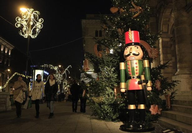 Ein großer Nussknacker steht neben einem Weihnachtsbaum auf einem beleuchteten Platz.