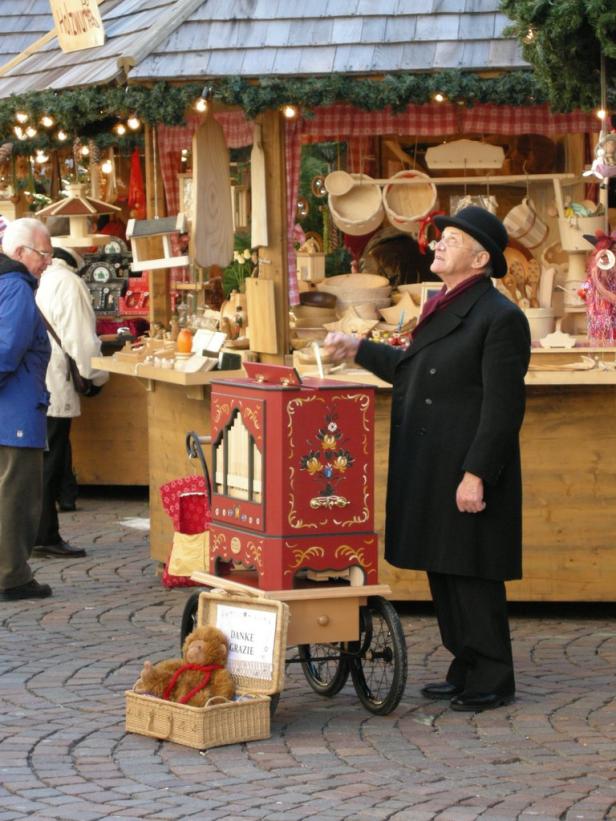 Ein Mann mit Drehorgel steht auf einem Weihnachtsmarkt.