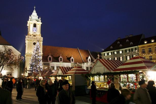 Ein Weihnachtsmarkt mit Menschenmenge vor einem beleuchteten Turm und Weihnachtsbaum.