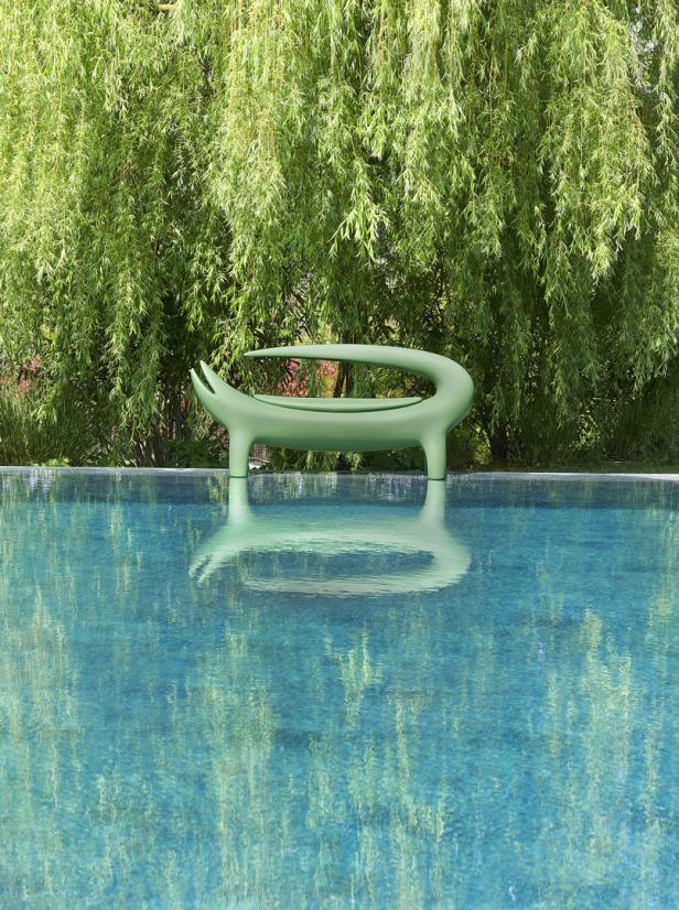 Eine grüne, moderne Liege steht am Rande eines Pools unter einem Baum.