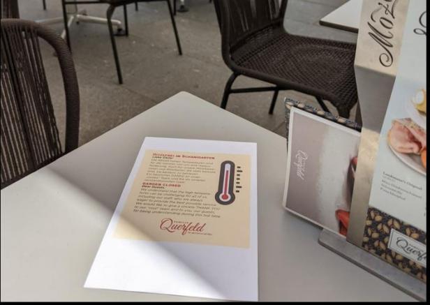 Ein Tisch im Außenbereich des Restaurants Querfeld mit einem Hinweis auf die Schließung des Schanigartens wegen Hitze.
