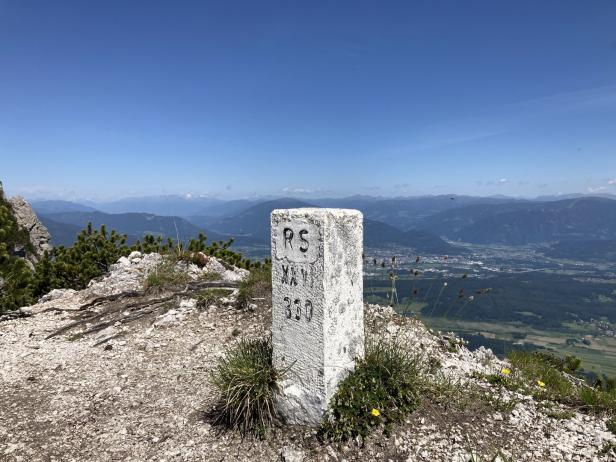 Ein Gipfelstein mit der Aufschrift „RS XXV 350“ vor einer Berglandschaft.