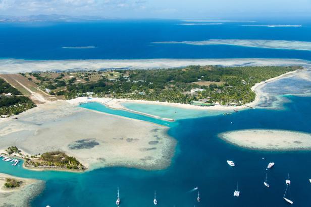 Luftaufnahme einer tropischen Insel mit Landebahn, türkisfarbenem Wasser und Segelbooten.