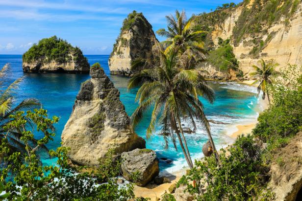 Türkisfarbenes Wasser umspült Felsen und einen Strand mit Palmen.