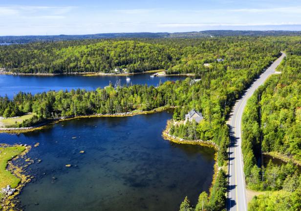 Luftaufnahme einer Küstenlandschaft mit blauem Wasser, grünen Bäumen und einer Straße.