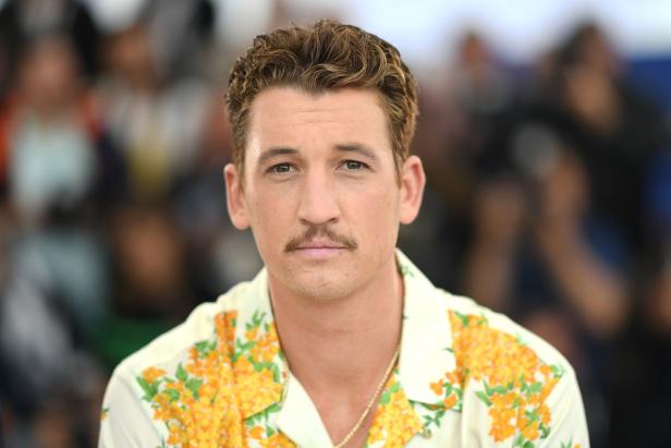 Ein Porträt von Miles Teller mit Schnurrbart und einem Hemd mit gelben Blumen.