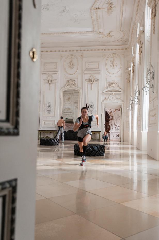 Eine Frau trainiert mit Gewichten in einem opulenten, weißen Saal.