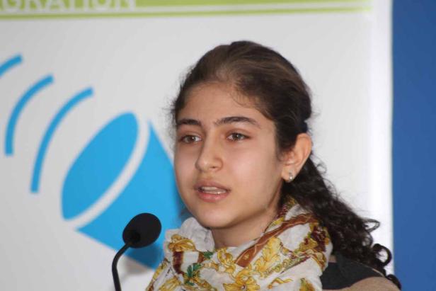 Eine junge Frau spricht vor einem Mikrofon mit einem gemusterten Schal.