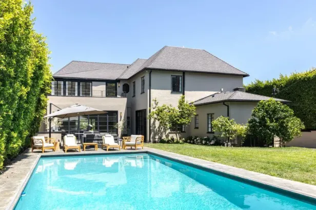 Ein Swimmingpool vor einem großen Haus mit Garten und Bäumen.