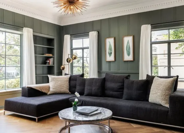 Ein Wohnzimmer mit einem grauen Sofa, einem Marmortisch und grünen Wänden.