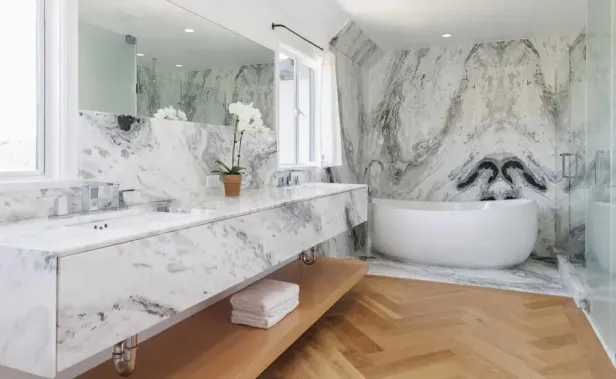 Ein Badezimmer mit Marmorwänden, einem Doppelwaschtisch und einer freistehenden Badewanne.