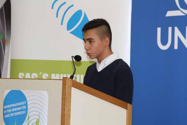 Ein junger Mann steht an einem Rednerpult und spricht in ein Mikrofon.