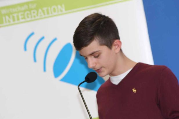 Ein junger Mann spricht bei einer Veranstaltung am Mikrofon.