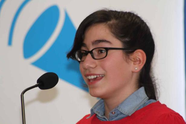 Ein junges Mädchen mit Brille spricht in ein Mikrofon.