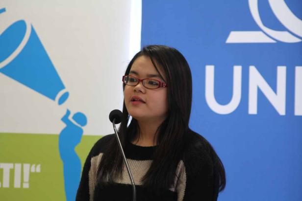 Eine junge Frau mit Brille spricht an einem Mikrofon vor einem blauen Banner.