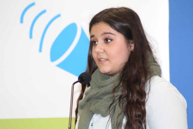 Eine junge Frau spricht bei einer Veranstaltung in ein Mikrofon.