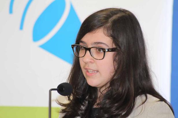 Eine junge Frau mit Brille spricht in ein Mikrofon.