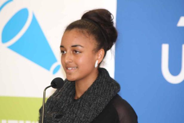 Eine junge Frau spricht bei einer Veranstaltung in ein Mikrofon.