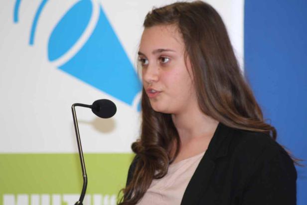 Eine junge Frau spricht bei einer Veranstaltung in ein Mikrofon.