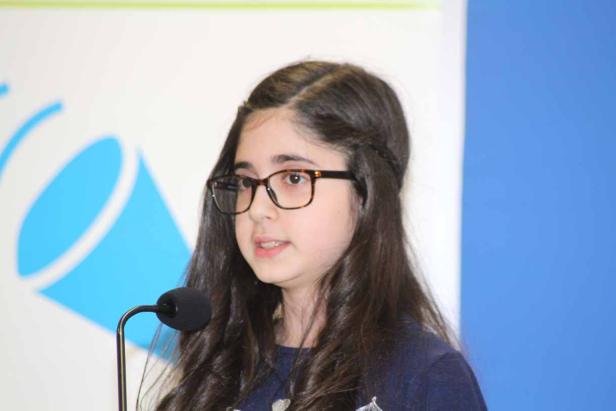 Ein junges Mädchen mit Brille spricht in ein Mikrofon.