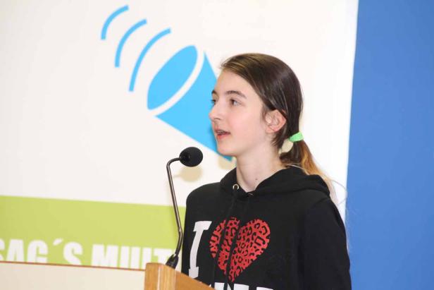 Ein junges Mädchen spricht an einem Rednerpult in ein Mikrofon.