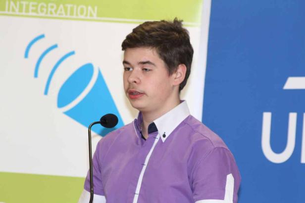 Ein junger Mann spricht bei einer Veranstaltung in ein Mikrofon.