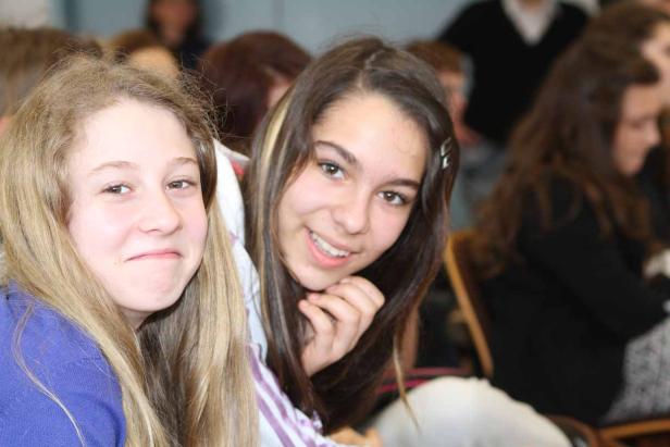 Zwei lächelnde junge Frauen sitzen nebeneinander in einem Raum.