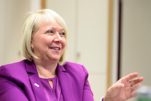 Eine lächelnde Frau mit blonden Haaren und einem lila Blazer.