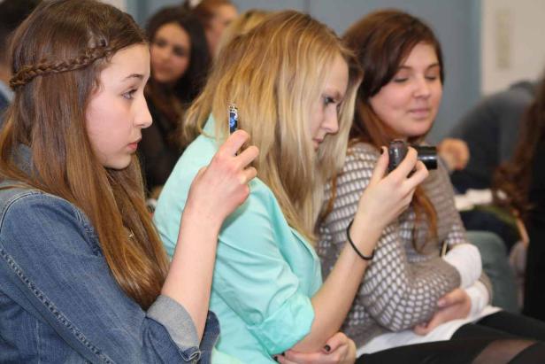 Drei junge Frauen sitzen nebeneinander und benutzen ihre Smartphones und eine Kamera.