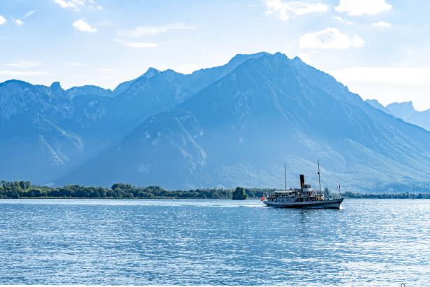 Ein Dampfschiff fährt auf einem See vor einer Bergkulisse.