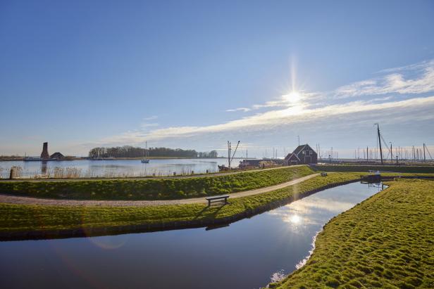 Ein Kanal fließt durch eine grüne Landschaft mit einem kleinen Hafen im Hintergrund.