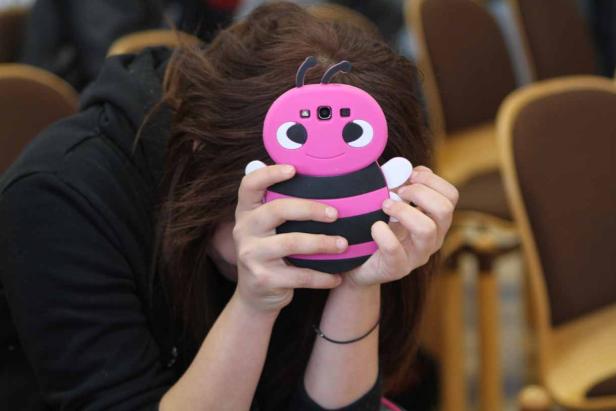 Ein Mädchen hält ein Smartphone mit einer rosafarbenen Bienenhülle vor ihr Gesicht.