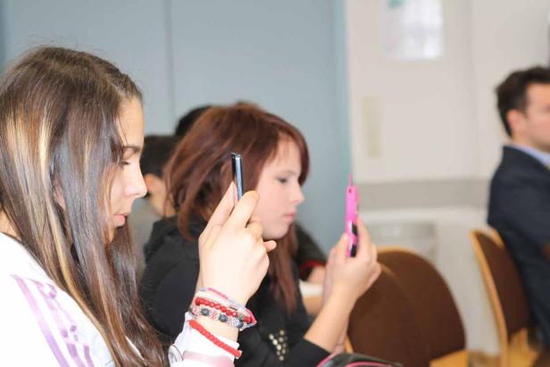 Zwei Mädchen sitzen nebeneinander und schauen auf ihre Smartphones.