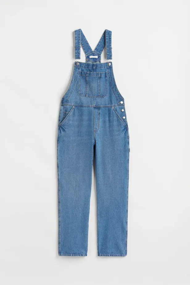 Eine blaue Jeanslatzhose hängt vor einem weißen Hintergrund.