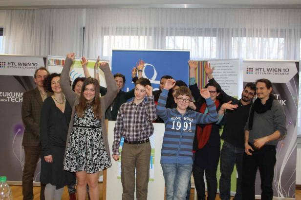 Eine Gruppe von Menschen posiert mit erhobenen Armen vor Bannern der HTL Wien 10.