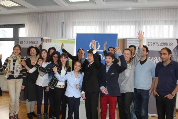 Eine Gruppe von Schülerinnen und Schülern posiert für ein Foto vor Bannern der HTL Wien 10.