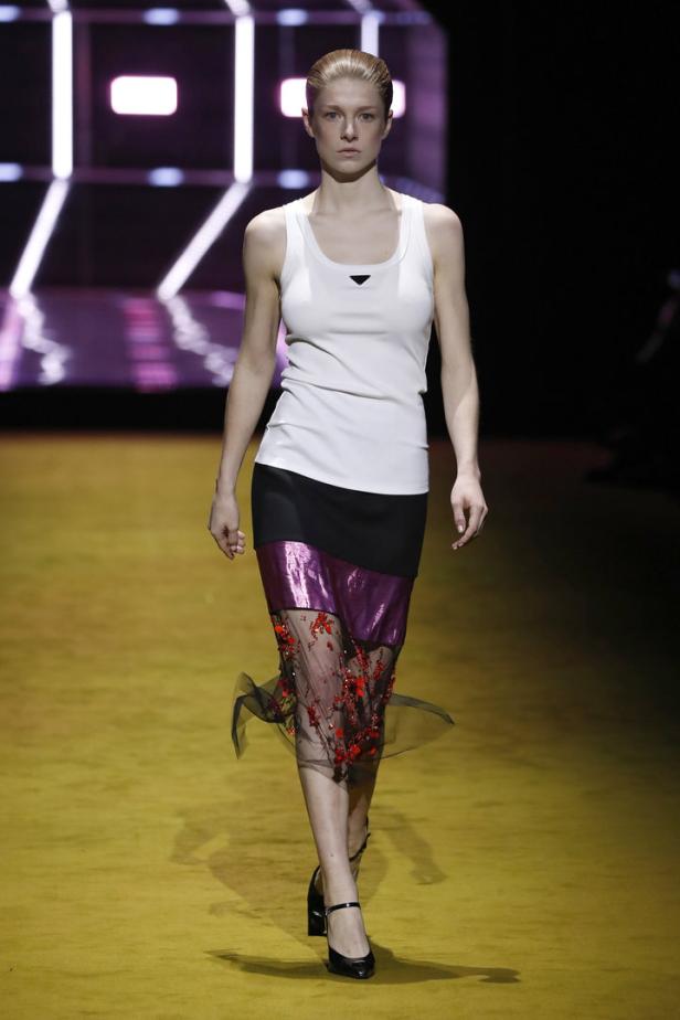 Eine Frau in einem weißen Tanktop und einem Rock mit floralen Details auf einem Laufsteg.