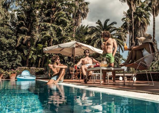 Eine Gruppe von Menschen entspannt sich mit Getränken an einem sonnigen Pool unter Palmen.
