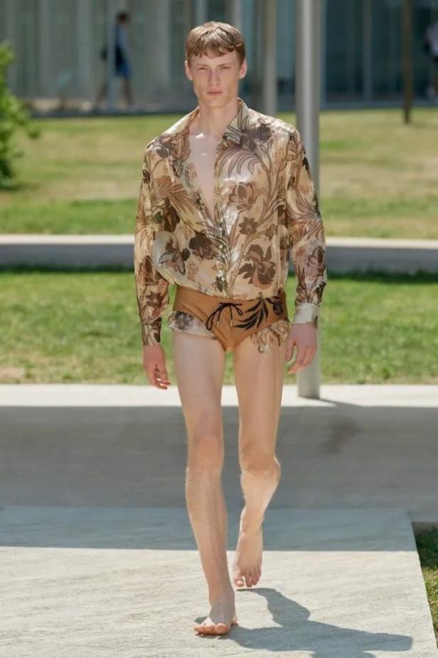 Ein Mann mit Hemd und Badehose läuft barfuß auf einem Gehweg.