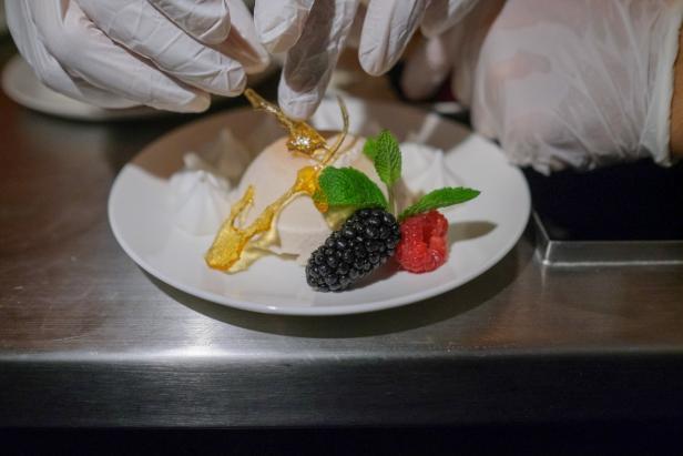 Ein Koch dekoriert ein Dessert mit Karamell, Brombeeren, Himbeeren und Minze.