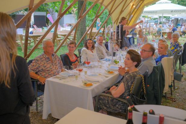 Eine Gruppe von Menschen sitzt an einem gedeckten Tisch unter einem Zelt.