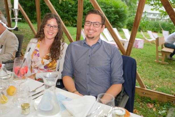 Ein lächelndes Paar sitzt an einem gedeckten Tisch im Freien.