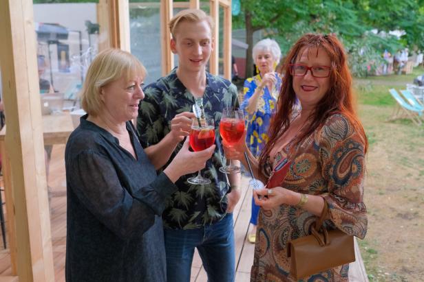 Drei Personen stoßen im Freien mit Aperol Spritz an.