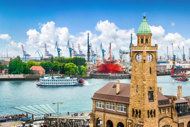 Blick auf den Hamburger Hafen mit der Turmuhr der Landungsbrücken und einem Raddampfer auf der Elbe.