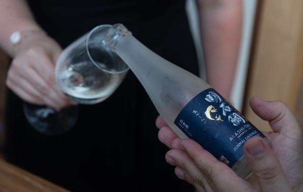Eine Person schenkt Akashi-Tai Junmai Daiginjo Sake in ein Glas ein.