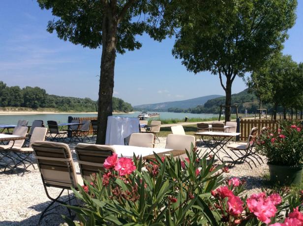 Ein Restaurantgarten mit Blick auf einen Fluss an einem sonnigen Tag.